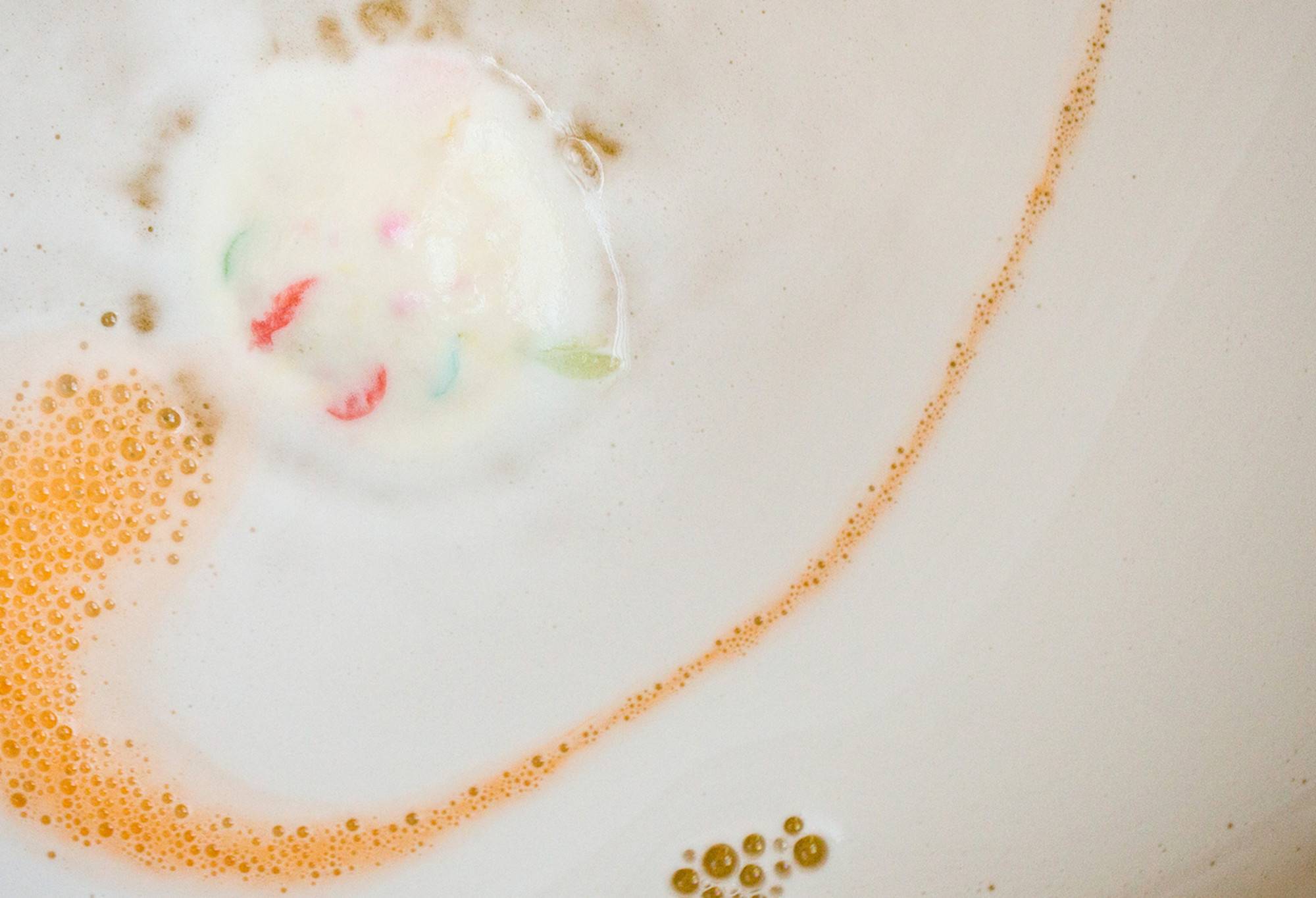The Dragons Egg bath bomb has almost fully dissolved leaving behind a thick, velvety white blanket of foam with colourful flecks and golden yolk-yellow water beneath. 