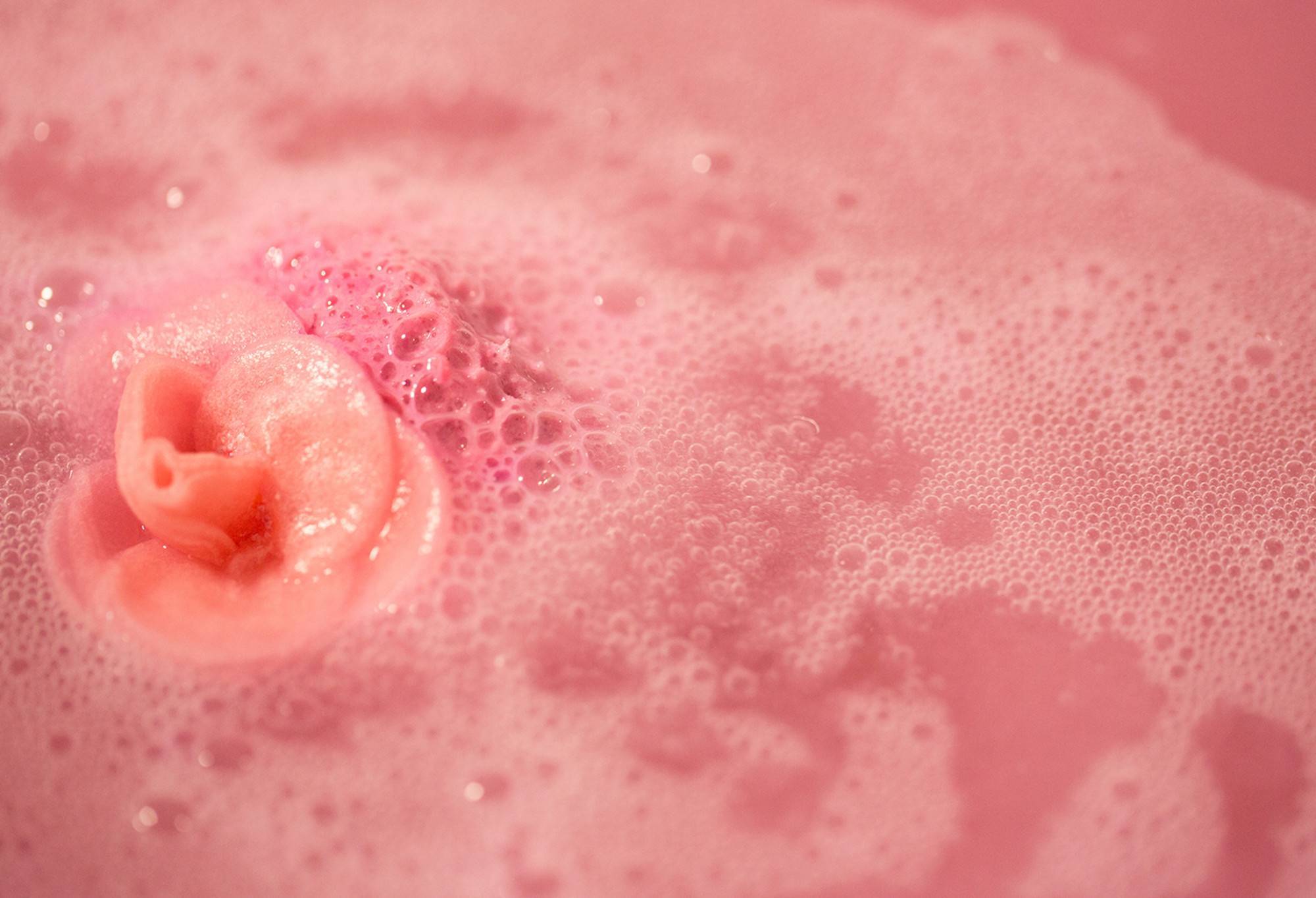 The Sex Bomb bath bomb has dissolved leaving behind silky, pink waters with the rice paper rose just visible over the blanket of pink bubbles. 