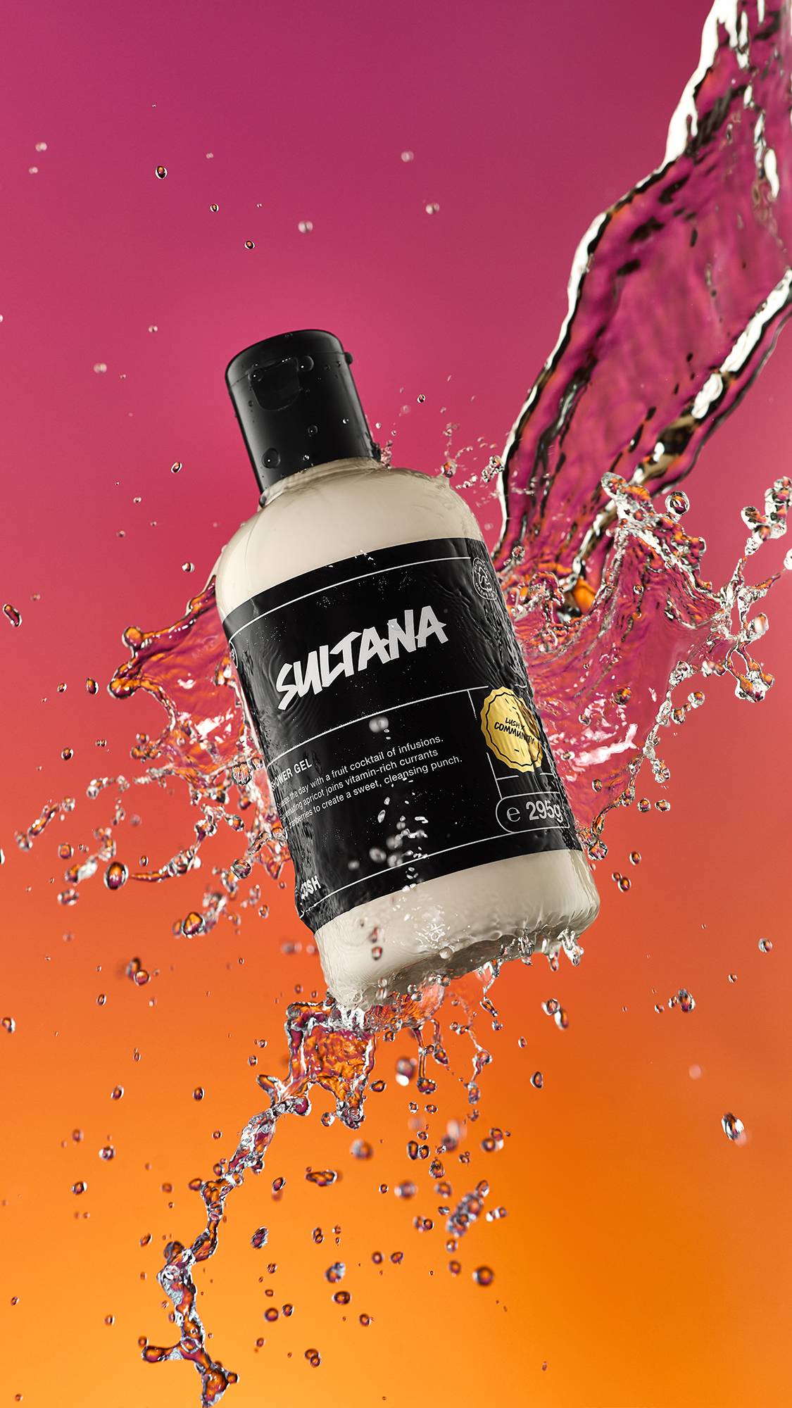 A high-definition action shot of the Sultana shower gel bottle mid-air being splashed by fresh water surrounded by droplets on a blurred pink and orange background.
