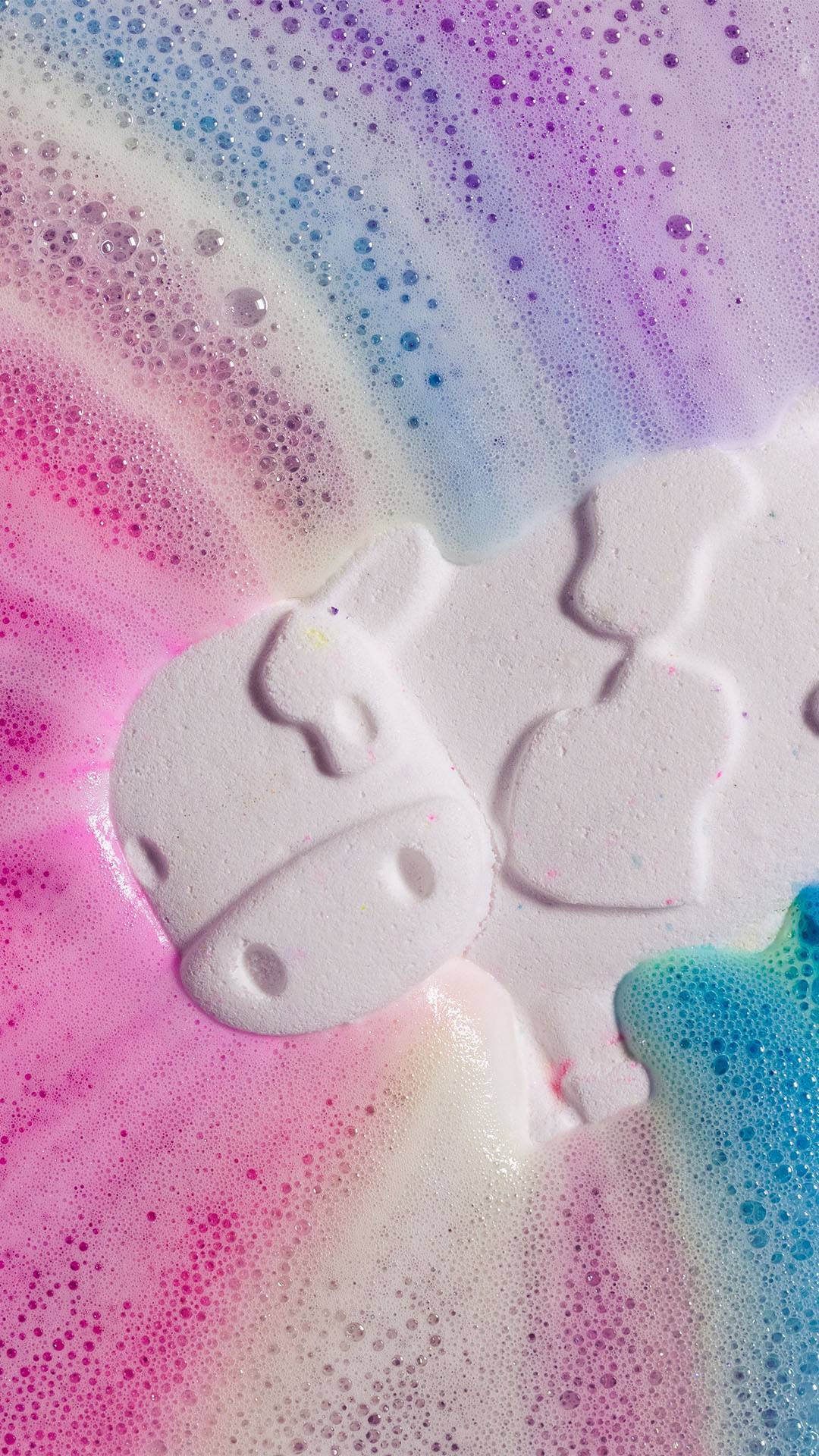 Toby's Magic Cow, a white cow-shaped bath bomb, lies back in a foamy rainbow-coloured water of its own fizzing creation.